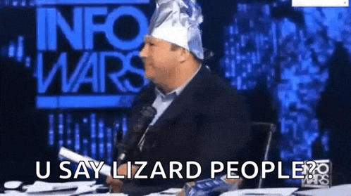 a man wearing a tin foil hat is sitting at a table with a microphone and says u say lizard people .
