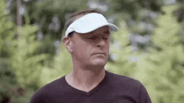 a man wearing a white visor and a black shirt is standing in a park .