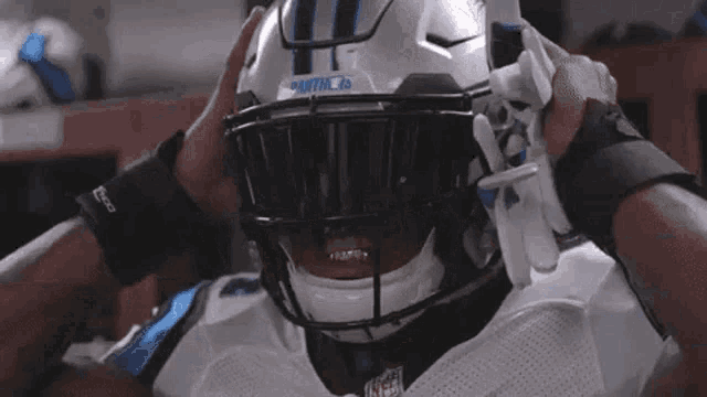a football player wearing a helmet and sunglasses is standing in a locker room .