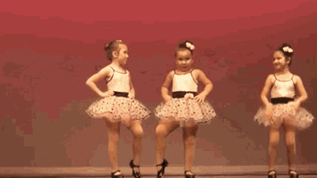 two little girls are dancing together on a stage while wearing tutus .