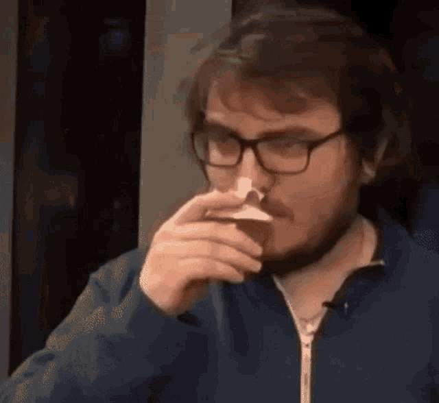 a man with glasses is blowing his nose with a napkin while sitting at a table .