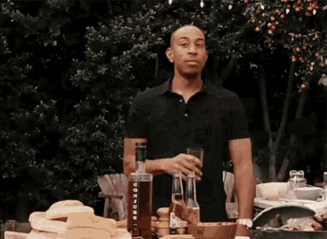 a man in a black shirt is standing in front of a table holding a glass and a bottle with the word cookden on it
