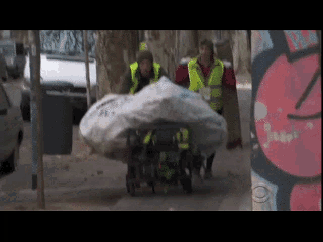 a man in a yellow vest is pushing a cart with a large bag on it