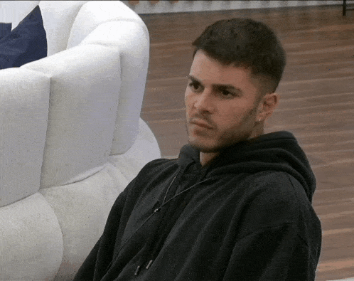 a man in a black hoodie is sitting on a couch