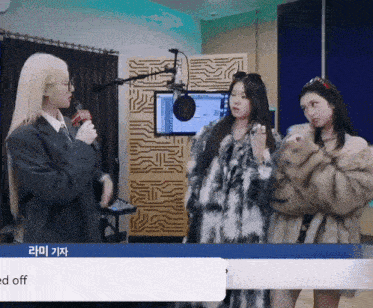 a woman in a fur coat talks into a microphone while another woman looks on