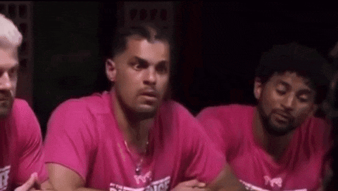 a group of men in pink shirts are sitting next to each other in a dark room .