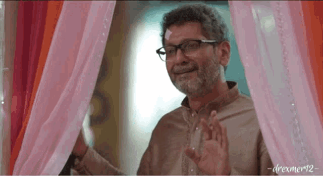 a man with glasses and a beard stands in front of pink curtains
