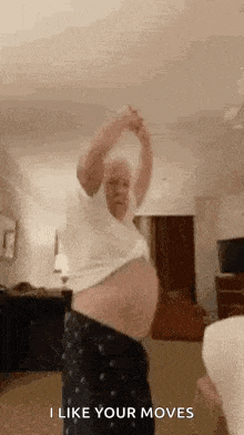 a pregnant woman is dancing in a living room while wearing pajamas and a white shirt .