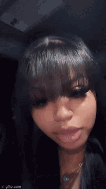 a woman with long black hair and bangs is wearing a necklace and looking at the camera .