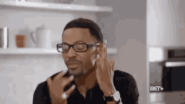 a man with glasses is talking on a cell phone in a kitchen .
