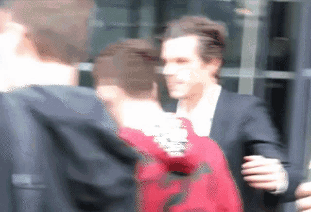 a blurry picture of a man in a suit talking to a man in a red shirt .