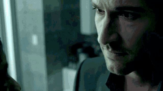 a close up of a man 's face in a dark room looking out a window .
