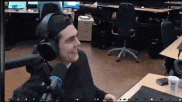a man wearing headphones and a hat is smiling in an office