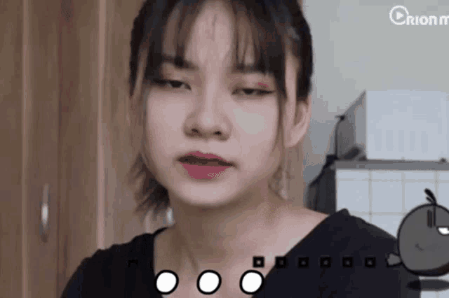 a girl is making a sad face in a kitchen with a cartoon apple in the background .