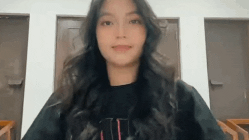 a young woman with long hair is standing in front of a door and smiling at the camera .