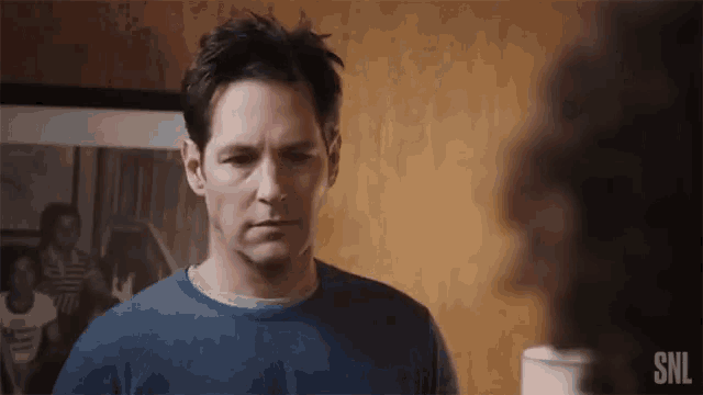 a man in a blue shirt with the snl logo on the bottom right