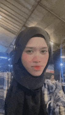 a woman wearing a black hijab and a plaid shirt is taking a selfie .