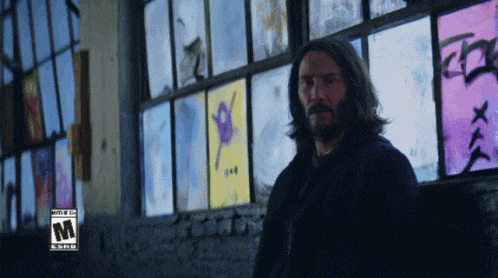 a man with a beard stands in front of a window with a sticker that says ' rated m ' on it