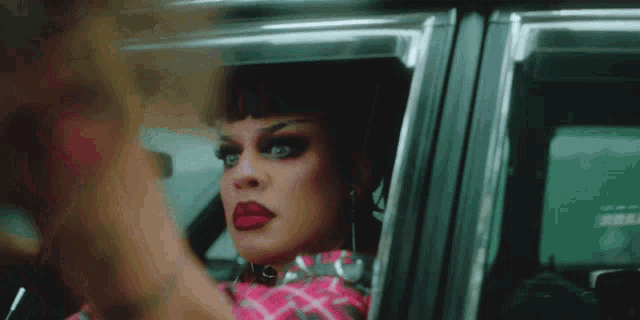 a woman in a pink plaid shirt is looking out of a car window