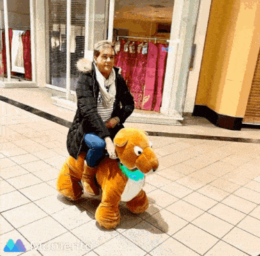 a woman is riding on the back of a stuffed animal with a momento logo behind her
