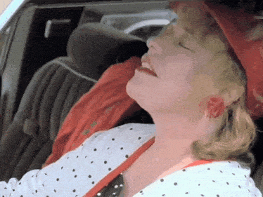 a woman in a red hat and polka dot shirt is sleeping in a car