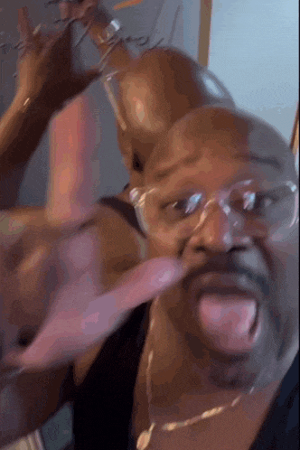 a man wearing glasses and a necklace is sticking his tongue out