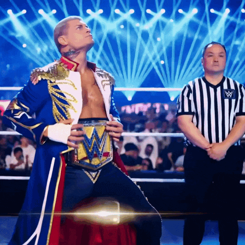 a wrestler with a belt that has the letter w on it stands in front of a referee