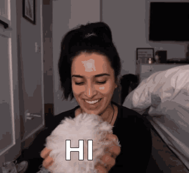 a woman is holding a small white dog and smiling with the word hi on her face