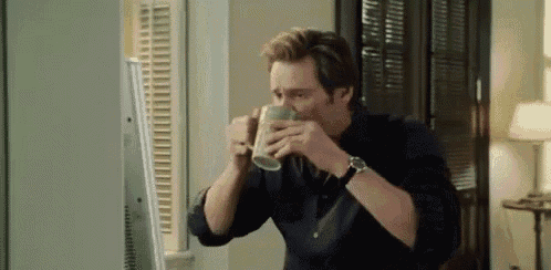 a man is drinking from a mug while sitting in front of a computer .