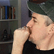 a man wearing a hat is sitting in front of a bookshelf .