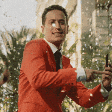 a man in a red suit and tie is taking a picture with his phone