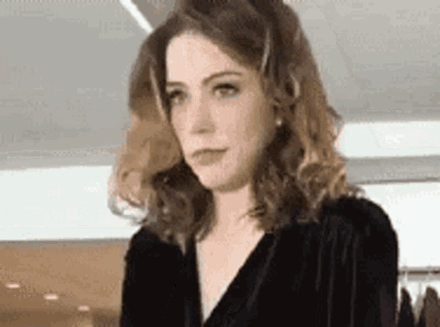 a woman with curly hair is wearing a black velvet dress and earrings .