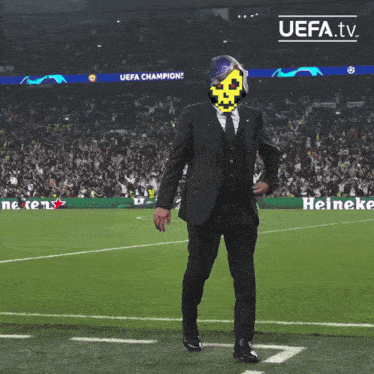a man in a suit and tie is walking on a soccer field with a heineken sign in the background