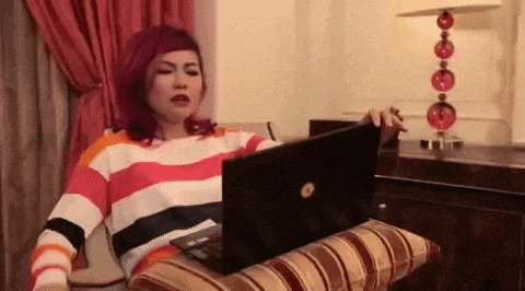 a woman with purple hair is sitting on a couch using a laptop computer .