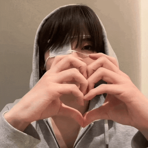 a person with a bandage on their eye making a heart with their hands