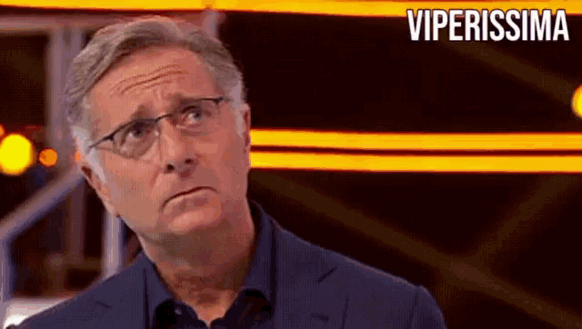 a man wearing glasses and a blue suit is standing in front of a sign that says viperissima
