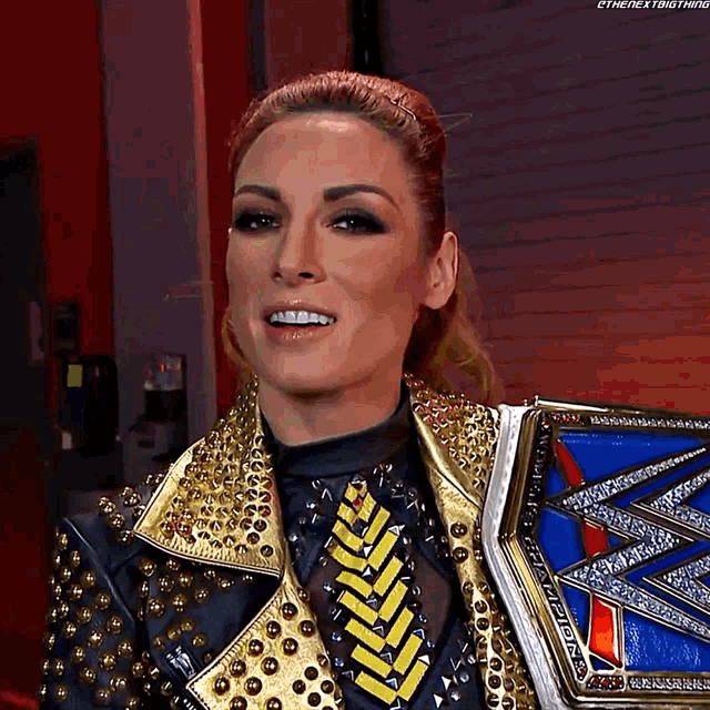 a woman is wearing a gold studded jacket and holding a championship belt