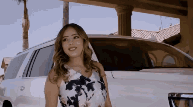 a woman in a floral dress is standing next to a white suv