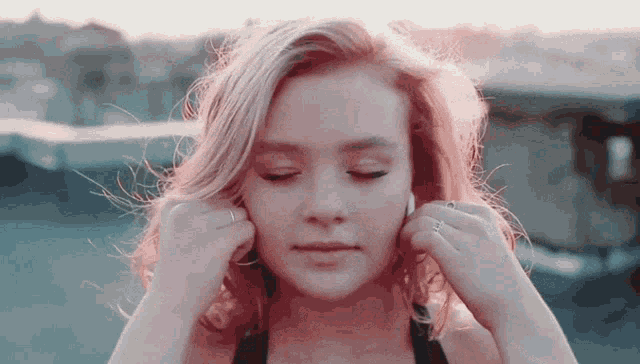 a woman adjusts her ear buds while listening to music with her eyes closed