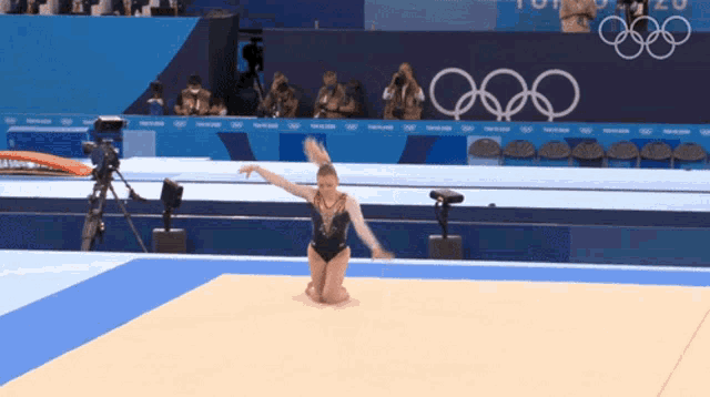 a female gymnast performs on the floor in front of a sign that says olympics