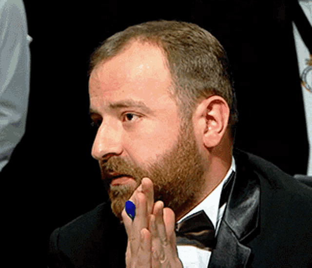 a man with a beard is wearing a black tuxedo and a bow tie
