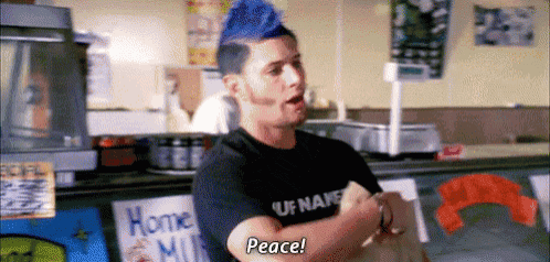 a man with a blue mohawk and a black shirt is standing in a store and says peace .