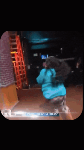 a woman in a blue jacket is dancing in front of a brick wall with the words " their father " on the bottom