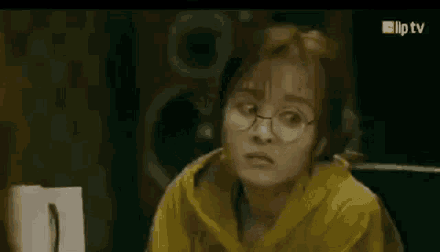 a woman wearing glasses and a yellow hoodie is looking at the camera .