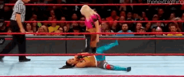 a woman is laying on the ground in a wrestling ring while a referee watches .