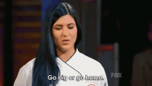 a woman with long black hair is standing in front of a staircase and saying `` go big or go home '' .