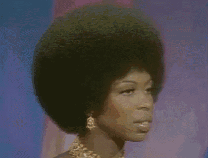 a woman with a very large afro is wearing a gold necklace and earrings .