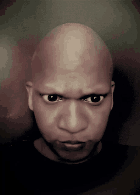 a man with a shaved head looks at the camera with a serious look on his face
