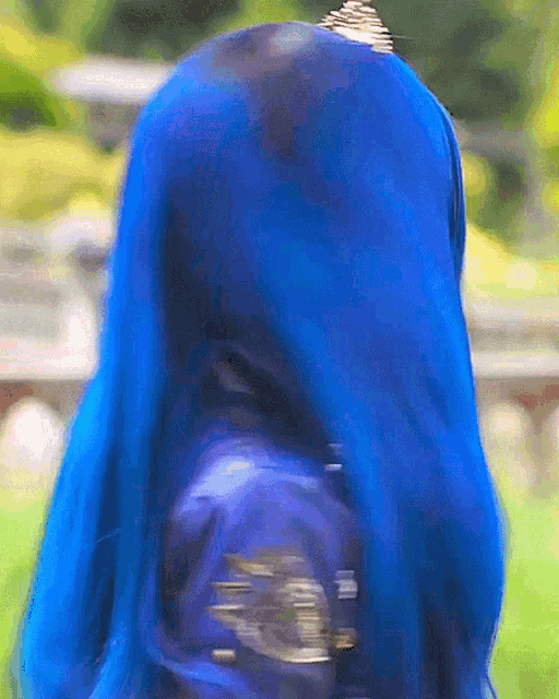 a woman with blue hair and a blue jacket is standing in the grass .