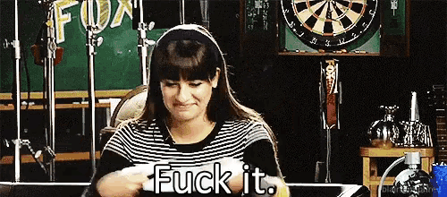 a woman is sitting in front of a dart board and holding a piece of paper that says fuck it .